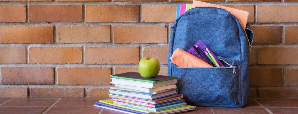 An apple atop of a stack of books and a bag