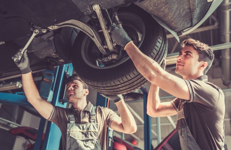 two mechanics repairing brakes of a car